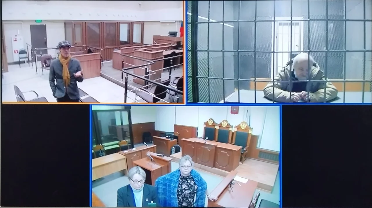 Монитор с тремя видеокадрами из суда; Александр Скобов виден за решёткой в одном из них.