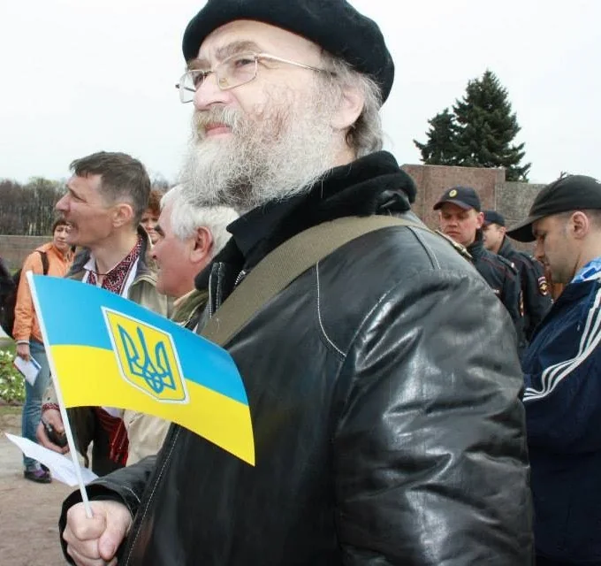 Александр Скобов в чёрной шапке держит небольшой флаг Украины.
